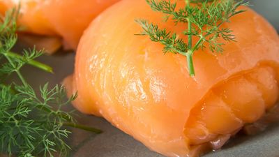 Close-up of sliced smoked salmon garnished with fresh dill on a gray plate, highlighting its vibrant orange color and smooth texture.