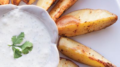 Golden-brown potato wedges arranged around a bowl of creamy sauce, garnished with a sprig of cilantro on top.