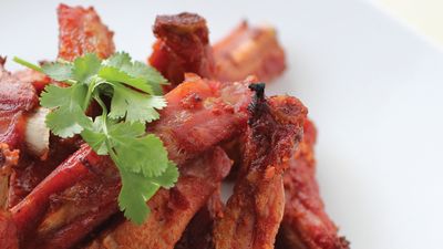 Close-up of crispy, grilled meat ribs garnished with fresh cilantro on a white plate.