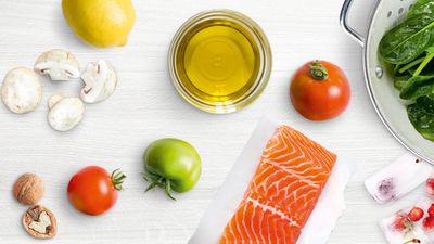 Fresh ingredients for cooking, including salmon, vegetables, oil, and lemon on a wooden table.