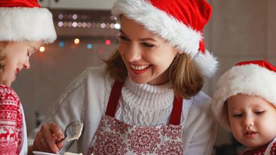 A festive scene featuring individuals wearing Santa hats and traditional holiday attire, preparing treats in a warmly decorated kitchen.