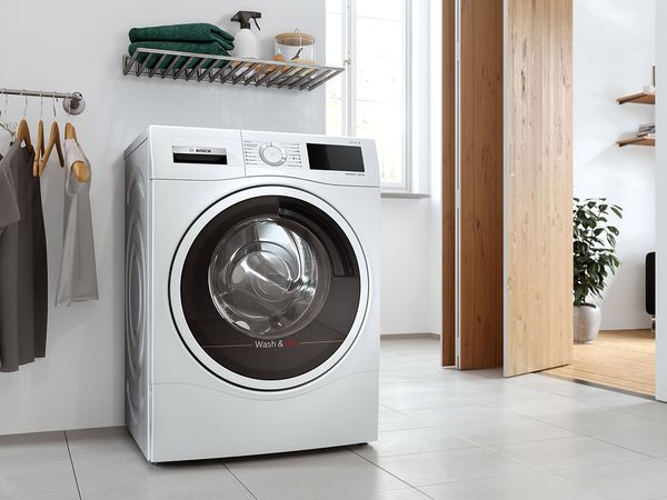 Washer dryer in an open laundry room next to a rack of hanging shirts