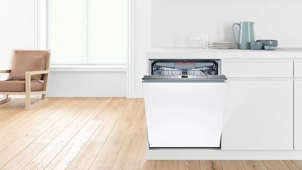 A woman is standing in the kitchen next to her Bosch dishwasher, which is slightly open. Behind her is the sink with the tap, which has a knot.