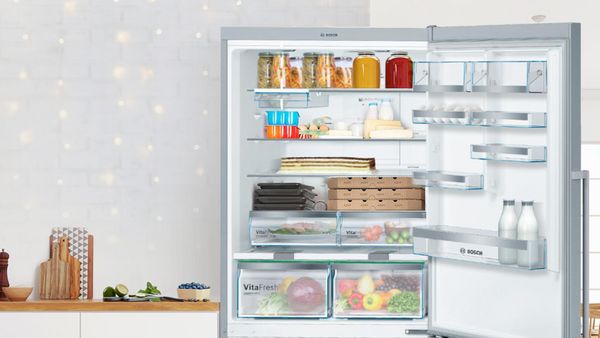 An open Bosch fridge filled with neatly arranged food items, showcasing fresh produce and jars.