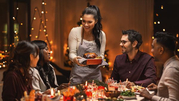 A woman serving food at a festive dinner table with family, surrounded by warm holiday decorations.