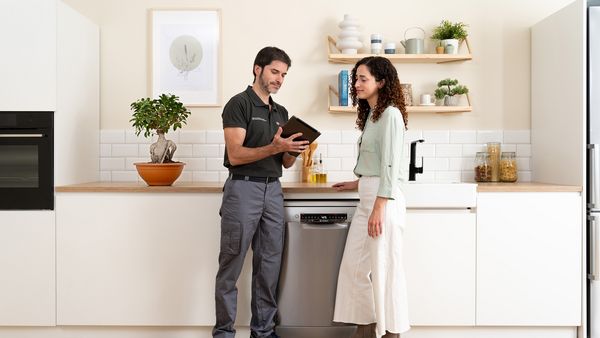 Een klant en een technicus praten met een iPad in een keuken voor de vaatwasser.