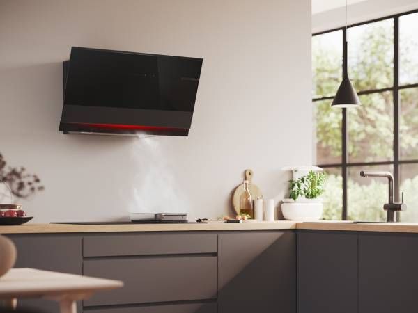 Moderne keuken met zwarte kasten, aan de muur gemonteerde tv en groot raam met uitzicht op groen.