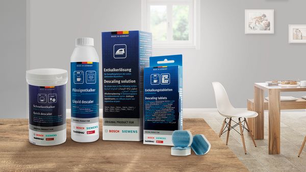 Cleaning products for descaling, featuring various bottles and tablets, displayed on a wooden table in a bright, modern kitchen.