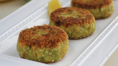 Three golden-brown veggie patties served on a white platter, garnished with a wedge of lemon for added zest.