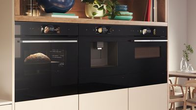 Stylish kitchen featuring three built-in black ovens and wood shelving for decoration. 