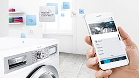 A user controls a washing machine with a smartphone featuring smart technology connectivity. 