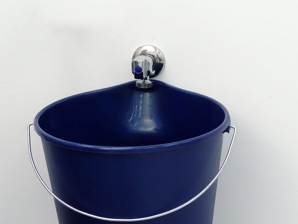 Blauwe emmer onder kraan waaruit tegen lage druk water stroomt