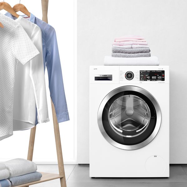 A modern washing machine beside neatly hung shirts and towels in a stylish laundry setting 