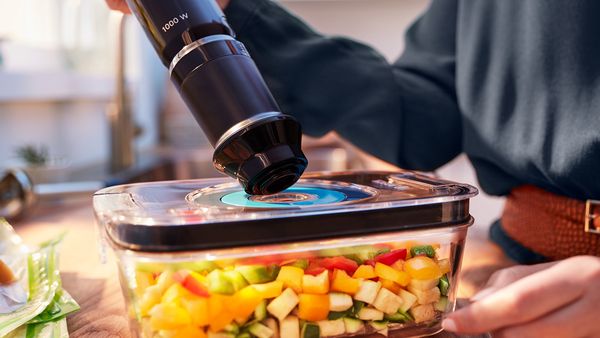 Boîte de conservation sous vide remplie de légumes frais conditionnée sous vide à l'aide d'un mixeur plongeant.