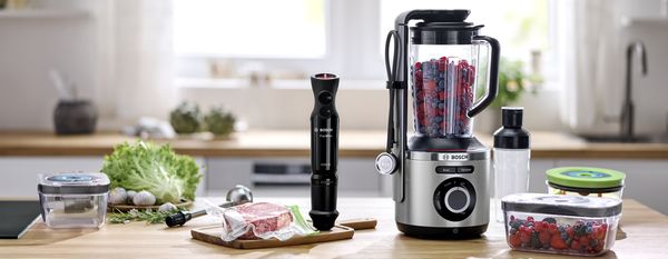 Blender VitaPower Serie 8 Bosch avec système de mise sous vide sur un plan de travail à côté de produits et d'accessoires de conditionnement sous vide.