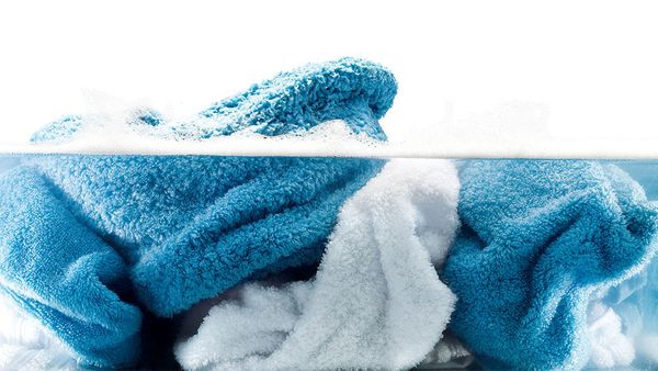 Dirty football in a laundry hamper in front of a front loader washing machine.