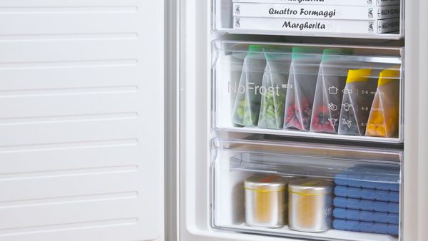 Inside a freezer, neatly organized with sealed bags of colorful vegetables and sauces, alongside pizza boxes and ice packs. 