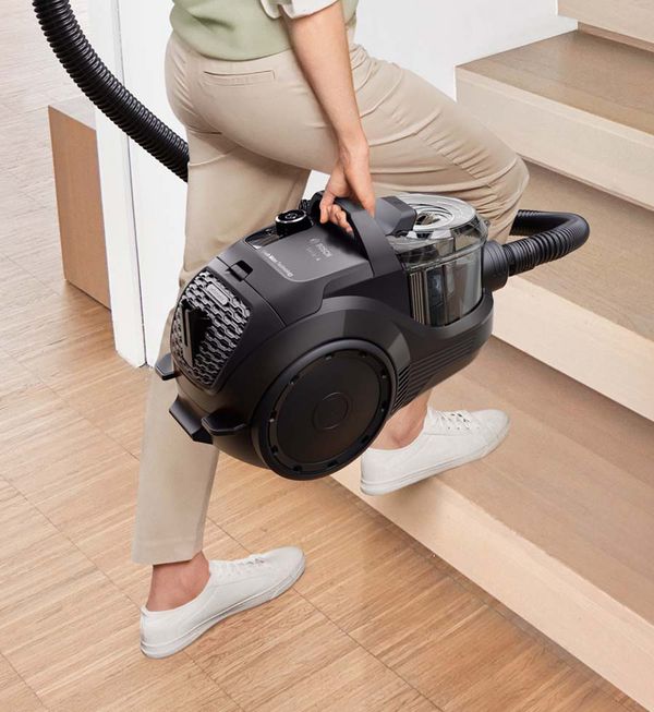Vrouw gaat de trap op met een sledestofzuiger zonder zak.
