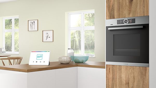  Kitchen with a built-in Bosch oven and a smart display on a wooden countertop, surrounded by natural light from windows. 