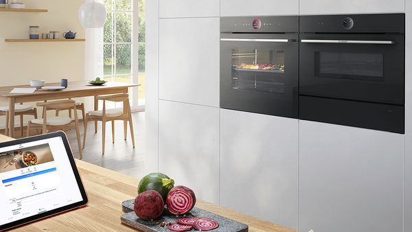 Elegante keuken met Serie 8 inbouwoven van Bosch met AirFry-functie en warmhoudlade. Diverse groenten in de oven. Meer groenten op een snijplank op een werkblad.