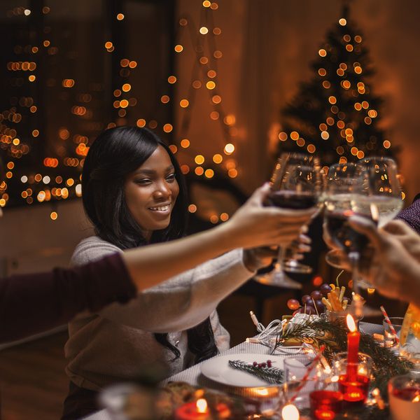 Close-up of friends toasting with glasses, celebrating a festive dinner adorned with holiday lights 