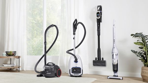 Four different vacuum cleaners are lined up in a bright hallway.