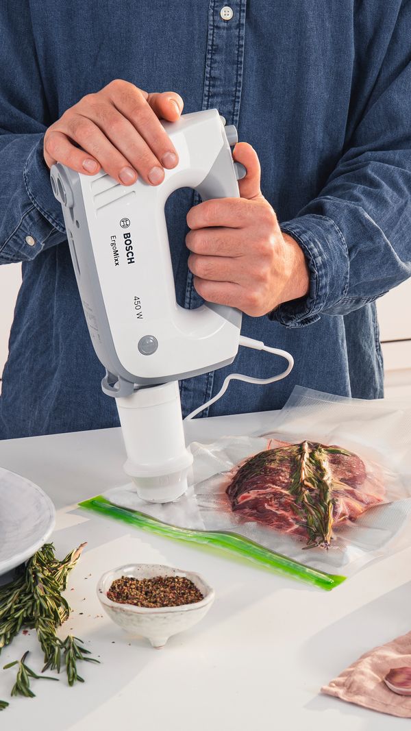 Une personne raccorde un batteur compatible à la valve d'un sac sous vide.