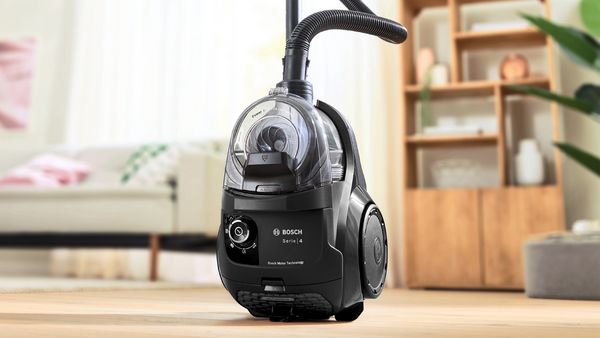 A Bosch cylinder vacuum stands upright in front of a cabinet in a living area.