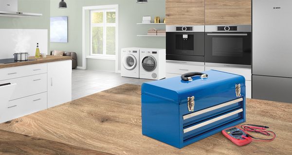 A bright kitchen scene featuring a blue toolbox and a multimeter on a wooden table, with modern appliances in the background.