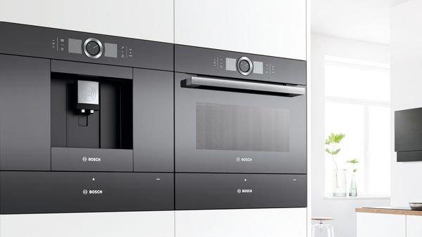 Inbouw volautomatische espressomachine naast een inbouwoven in een witte keuken.