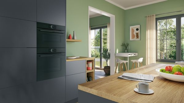 Moderne keuken met groene muren, houten aanrecht, zwarte kasten, en natuurlijk licht van ramen.