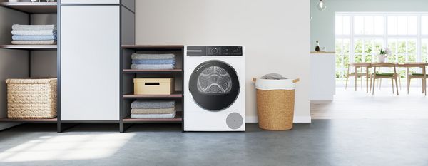 Tumble dryer beside shelves of towels, with a basket for laundry in a modern laundry area. 