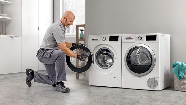 Un homme répare un lave-linge dans une buanderie bien éclairée.