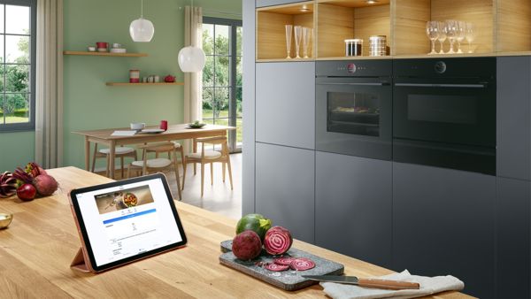 
       iPad, розміщений на кухонному острові, демонструє рецепт, на фоні інтегровані духові шафи, створюючи атмосферу.
      