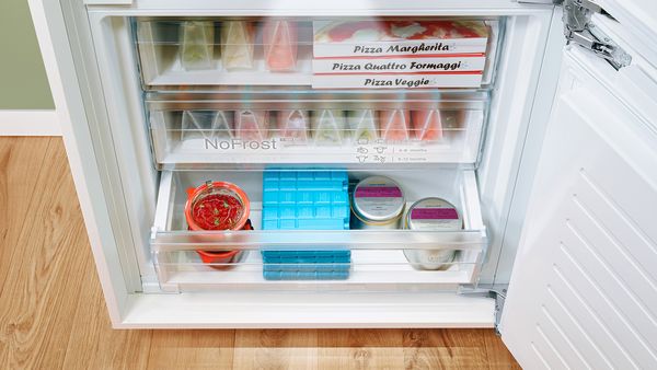 The door of a fridge's freezer section is open to reveal the neatly organised food in drawers.