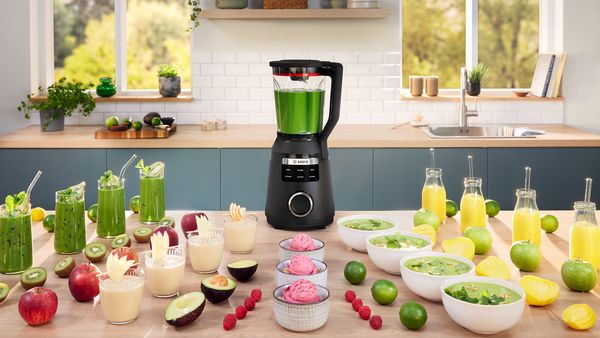 Een VitaPower Serie 6 op een keukentafel, omringd door enkele glazen en kommen met verschillende smoothies, milkshakes, roomijs en stukken fruit.