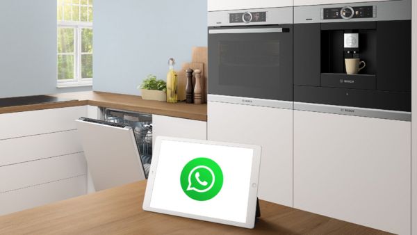A modern kitchen featuring Bosch appliances and a tablet displaying the WhatsApp logo on a wooden countertop.