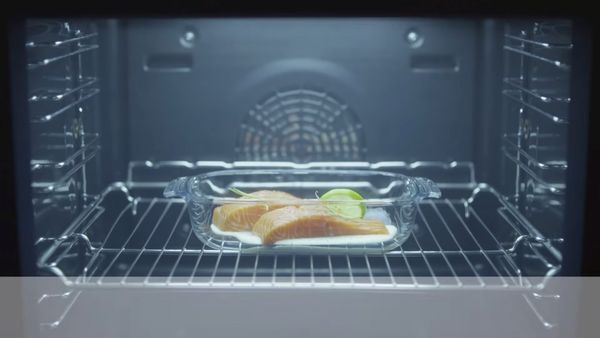 Baked goods on oven rack, illuminated by interior oven light, with reflective surfaces and heating elements visible. 