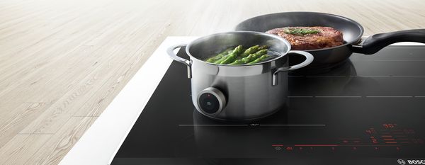 Cooking pots on induction cooktop, asparagus and steak, modern kitchen appliance. 