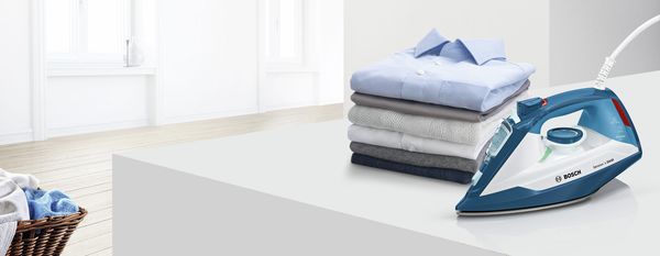 Ironing board with folded clothes, iron, and laundry basket in a bright, minimalist room. 