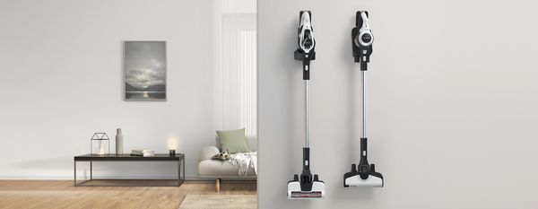 Two modern cordless vacuum cleaners are mounted on a wall in a stylish living room with a minimalist design and soft lighting 